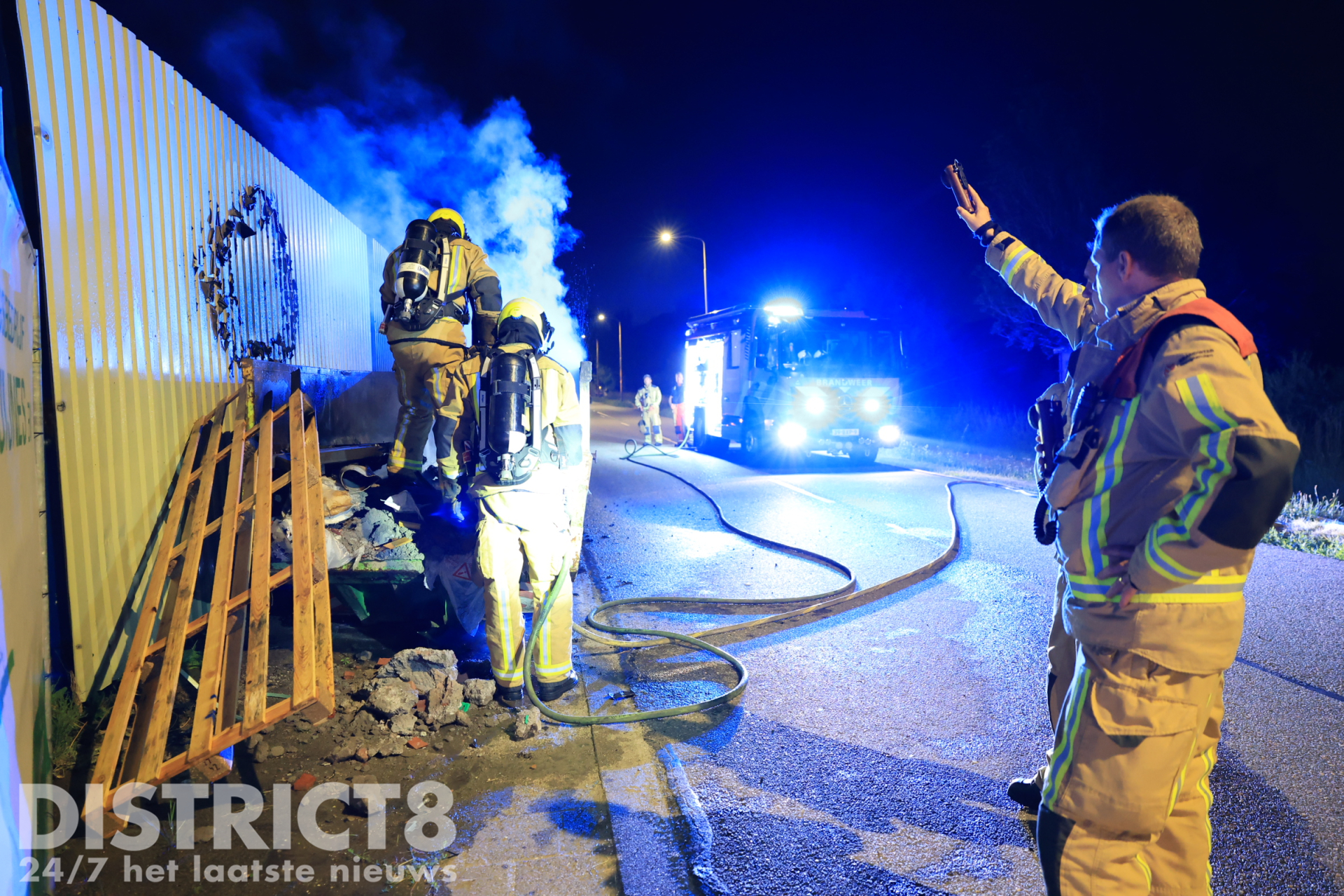 Brandweer blust felle containerbrand tegen hekwerk van scheepswerf Rotterdamseweg Delft